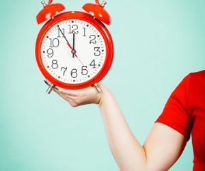 Woman hand holding old fashioned decorative red big clock watch, studio shot on blue background.